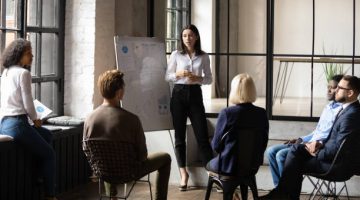 Confident lady business trainer coach leader give flip chart presentation consulting clients teaching employees training team people speaking explaining strategy at marketing workshop concept